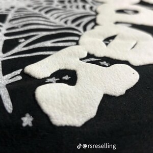 Puede incluir: Primer plano de un textil negro con un dise&ntilde;o blanco en relieve que presenta una calavera estilizada y una telara&ntilde;a. El dise&ntilde;o incluye estrellas y un elemento similar a un &aacute;rbol. El identificador de Instagram @rsreselling es visible.