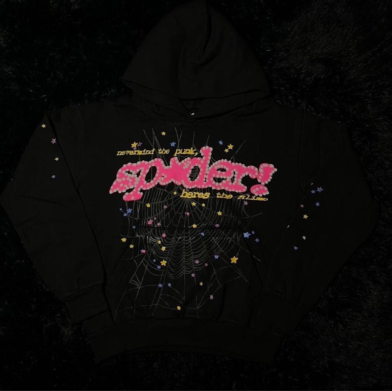 May include: Black hooded sweatshirt with the word "Spider" in pink, embellished with small pink flowers. The design includes a spiderweb and the phrases "nevermind the punk" and "heres the slime" in a playful font. Colorful stars are scattered around the design.