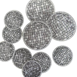 May include: A collection of nine circular embroidered patches featuring a silver disco ball design. Each patch displays a grid of square tiles with a glittery finish and white starburst accents, all bordered by a stitched silver edge.
