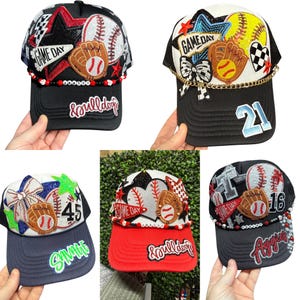May include: Baseball caps with baseball-themed decorations. Each cap features baseballs, gloves, and stars. The caps have different colour schemes, including black, red, and navy blue, with text such as "Game Day" and team names.