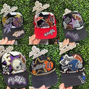May include: Six custom baseball caps with team-themed designs. Each cap has a black peak and a white or red crown, decorated with football motifs, stars, team names, and numbers. The caps are embellished with rhinestones and beads, creating a unique look.