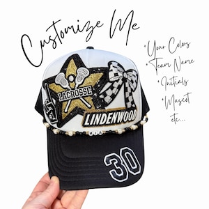 May include: Black and white baseball cap with gold accents. The cap features the word "LACROSSE" and "LINDENWOOD" on the front, along with a star and bow design. The number "30" is displayed on the side. The text "Customize Me" is written on the top.