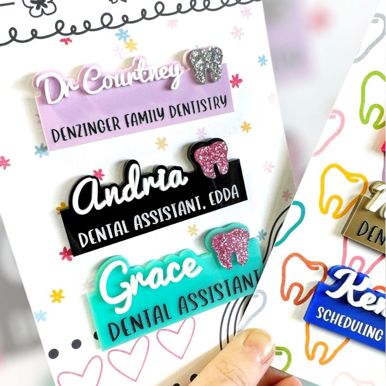 May include: A collection of personalized dental office name badges. The badges feature names like "Dr. Courtney," "Andria," and "Grace," along with titles and a tooth graphic. The badges are in various colors, including lavender, black, and teal.