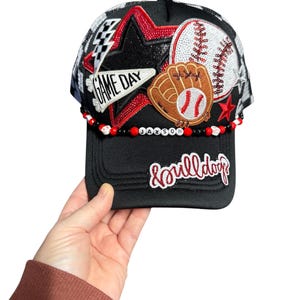 May include: Black baseball cap with a mesh back, featuring a star, baseball, and glove design. The cap has the text "GAME DAY" and "&bulldogs". A beaded band spells out "JAXSON".