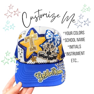 May include: A white and blue trucker hat featuring a large yellow star with a letter T, a blue and white checkered bow, a drum set patch, and the text "Golden Wave" and "Luke". A beaded strand reads "THE LONG BLUE LINE" with additional text.