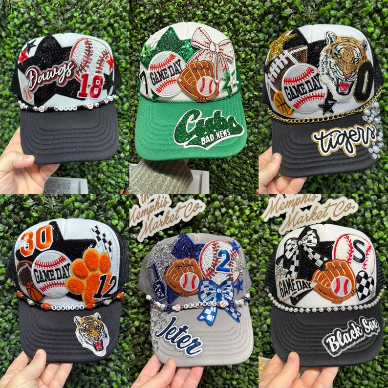 May include: Six baseball-themed trucker caps with mesh backs and curved brims. Each cap is adorned with baseballs, gloves, and team names such as "Dawgs," "Cubs," and "Tigers." The caps are decorated with beads and sequins.