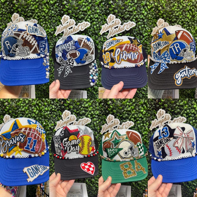 May include: Eight baseball caps with sports-themed designs. Each cap has a different team name or logo, decorated with beads, bows, and glitter. The caps have a mesh back and a curved peak. The text "GAME DAY" is visible on some caps.