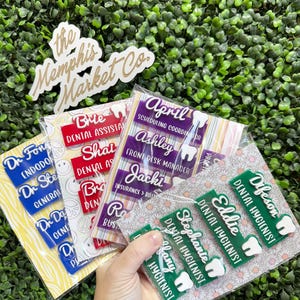 May include: A collection of name badges for dental professionals. The badges are in various colors, including red, purple, and green, with white text. Some badges include a tooth graphic. The Memphis Market Co. logo is also visible.