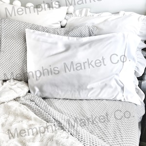 May include: White bedding with a gray and white geometric pattern. The bedding is arranged on a bed with a white fluffy blanket and white pillows. The text "Memphis Market Co." is visible on the pillows and blanket.