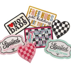 May include: A collection of seven embroidered patches featuring various designs including a heart with a red heart icon, text reading I HOT DADS, FREE HUGS just kidding NOT TOUCH ME, SUSPECT RUNS ON ALAN, and Spoiled BY MY BLUE COLLAR MAN.