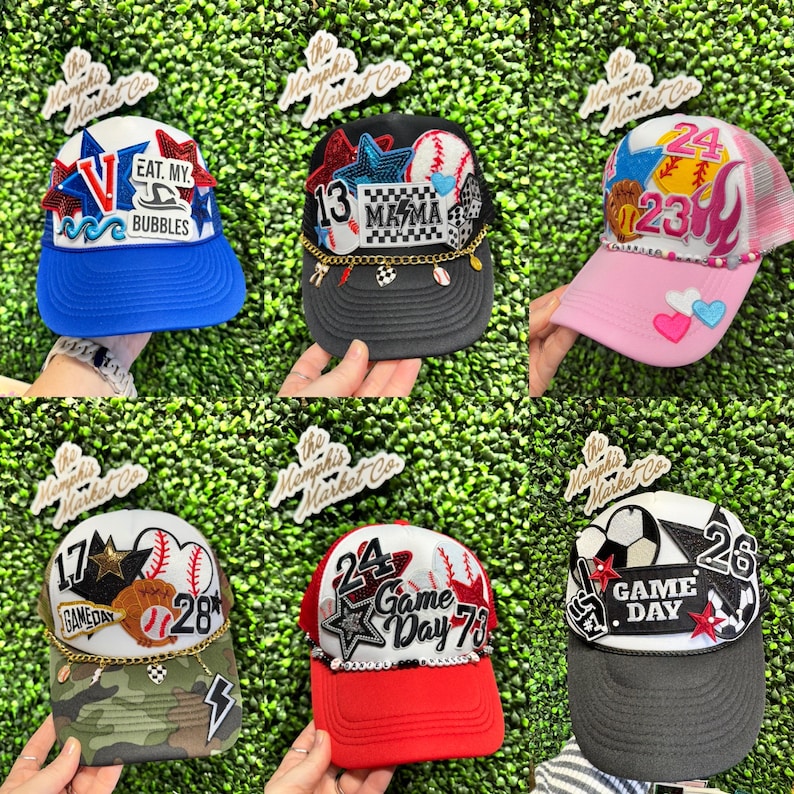 May include: A selection of baseball caps with diverse designs and text. One cap is blue with "EAT. MY. BUBBLES" text. Others feature numbers, stars, baseballs, and the words "MAMA" and "GAME DAY".