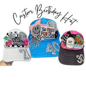 May include: Three custom birthday hats. A white hat with a silver star and cherries, a blue hat with a smiley face and the number 40, and a black and pink hat with the number 30. Each hat has decorative embellishments.