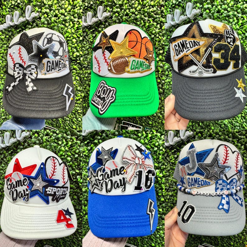 May include: Selection of baseball caps with sports-themed decorations. Each cap has a different colour scheme, with details such as stars, baseballs, and the words "Game Day" and numbers. The caps have curved peaks and adjustable fastenings.