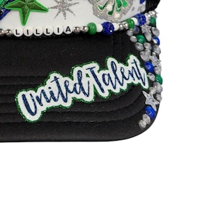 May include: A black trucker hat featuring a white front panel adorned with green star patches, silver glitter stars, and a beaded trim spelling LILLIA. The black brim displays a green and blue glitter patch with the text United Talent.