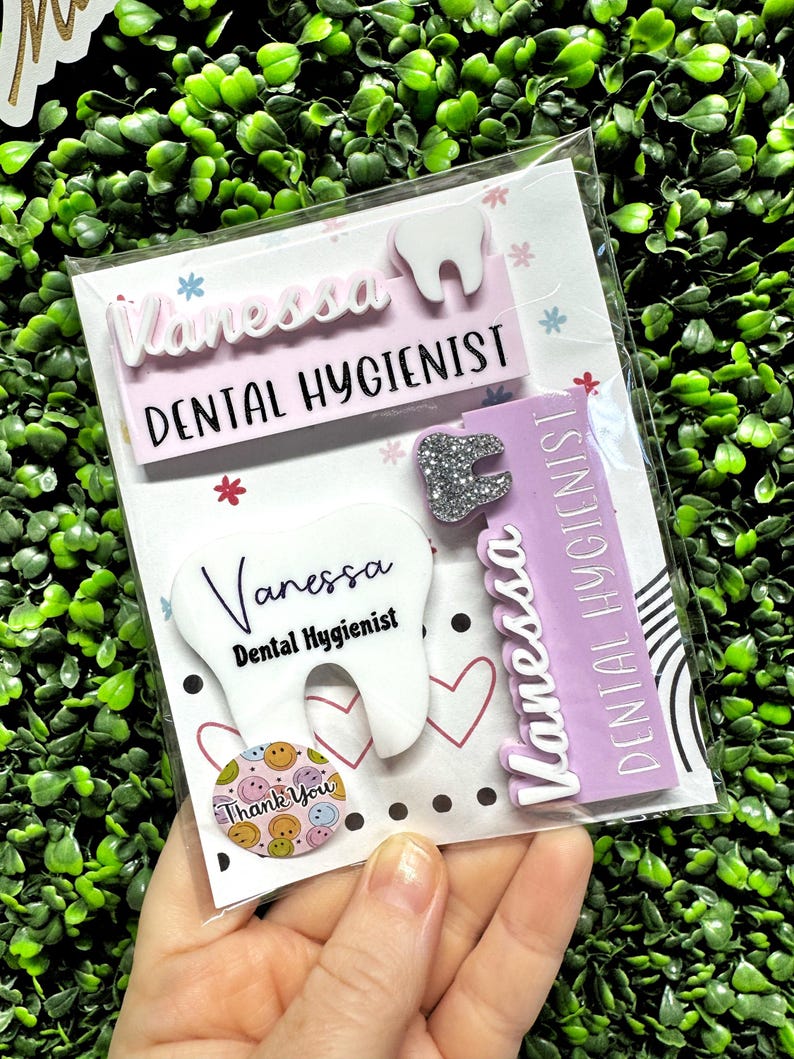 May include: A clear plastic package containing dental-themed accessories. Includes a white tooth-shaped pin, a name tag with the name "Vanessa" and the title "Dental Hygienist", and a small button with smiley faces and the words "Thank You".