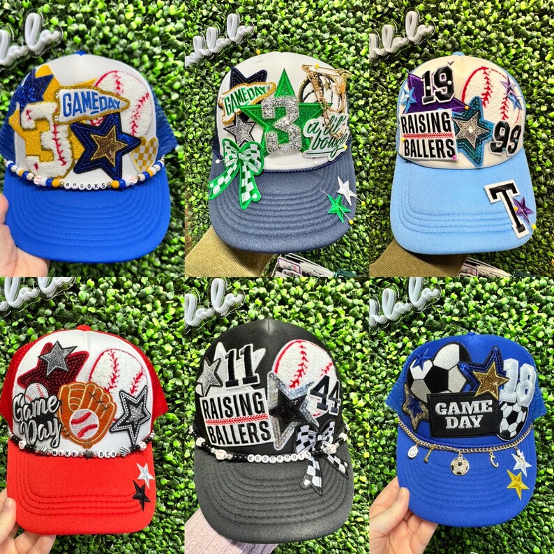 May include: Six baseball caps with assorted designs. The caps display text such as "Game Day" and "Raising Ballers", alongside baseballs, stars, and other decorations. The caps come in various colour schemes, including blue, red, and black.