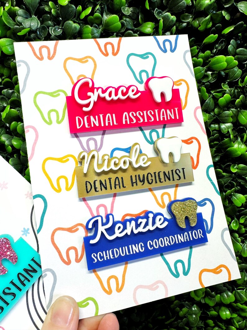 May include: A white card with a colorful tooth pattern, featuring three name badges for dental professionals. The badges are in pink, gold, and blue, with names and job titles like "Dental Assistant" and "Dental Hygienist".