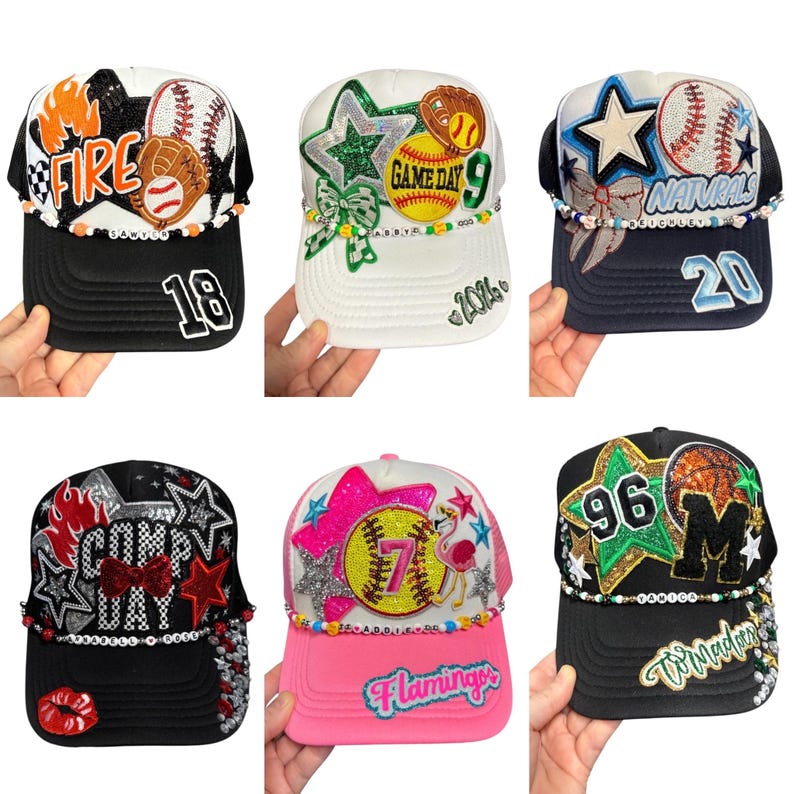 May include: Six baseball-themed trucker caps with different designs. One cap has "FIRE" and "18", another has "GAME DAY 9" and "2026", and another has "NATURALS" and "20". Other caps have "COMP DAY", "7 Flamingos", and "96 M Tomader".