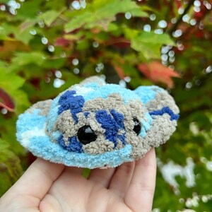 May include: A small, blue, gray, and white plush toy shaped like a stingray. The toy has large black eyes and a fuzzy texture.