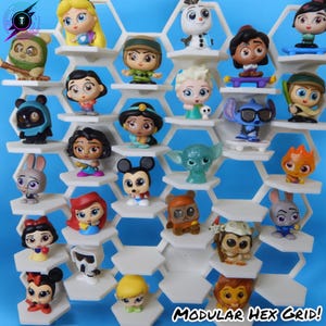 May include: A white hexagonal display shelf with 24 small figurines of Disney characters. The shelf is labeled "Modular Hex Grid!" at the bottom. The figurines include characters like Mickey Mouse, Minnie Mouse, Snow White, Ariel, Jasmine, Aladdin, Elsa, Anna, Olaf, Stitch, and more.