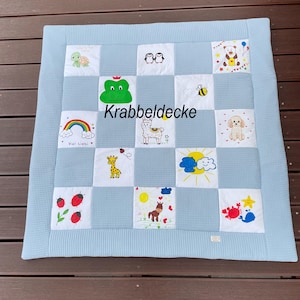 Könnte beinhalten: Eine hellblaue Krabbeldecke mit Waffelstruktur und einem Raster aus weißen Stoffquadraten. Jedes Quadrat zeigt bunte gestickte Illustrationen, darunter eine Schildkröte, Pinguine, einen Bären, einen Frosch, eine Biene, einen Regenbogen, ein Lama, einen Hund, eine Giraffe, Sonne, Wolken, Marienkäfer, ein Pferd, einen Krebs, einen Stern und einen Wal. Der Text Krabbeldecke ist mittig platziert.