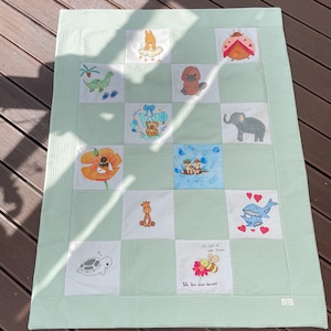 Könnte beinhalten: Eine hellgrüne Decke mit Waffelstruktur und einem Raster aus weißen Stoffquadraten. Jedes Quadrat zeigt gestickte Tierillustrationen, darunter eine Schildkröte, eine Giraffe, einen Elefanten, ein Schnabeltier, einen Marienkäfer und einen Wal.