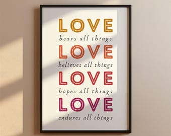 May include: A white framed print with the word "LOVE" repeated four times in different colors, each with a phrase below it. The colors are orange, red-orange, red, and pink. The phrases are "bears all things", "believes all things", "hopes all things", and "endures all things".