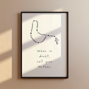 May include: Black framed art print featuring a hand-drawn rosary and cross. The text "When in doubt, call your Mother" is written below the rosary in a simple, handwritten style. The background is a neutral off-white.