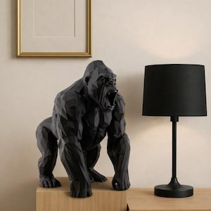 Puede incluir: Una escultura de gorila geométrico negro con la boca abierta se encuentra sobre un mueble de madera. A la derecha hay una lámpara negra con una pantalla negra. Un cuadro con marco dorado cuelga de la pared.