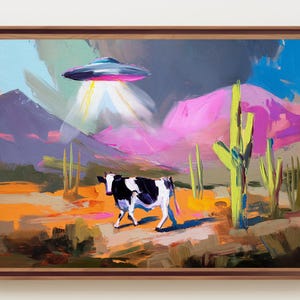 May include: A framed oil painting depicting a black and white cow standing in a desert landscape with saguaro cacti, purple and pink mountains, and a metallic flying saucer hovering above, casting a bright yellow light beam down onto the ground.