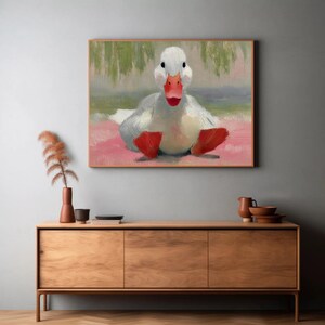 Puede incluir: Pintura al &oacute;leo de un pato blanco con pico y patas rojos, sentado sobre una superficie rosa. El pato est&aacute; centrado en el marco, con un fondo borroso de tonos verdes y azules. La obra de arte est&aacute; enmarcada en un marco de madera.
