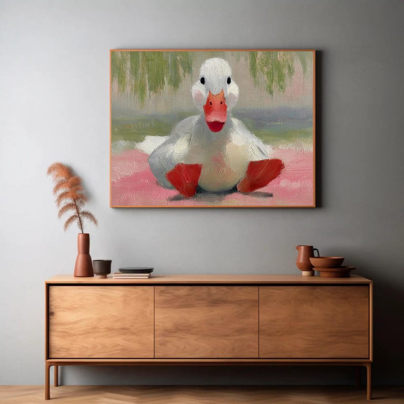 Puede incluir: Pintura al &oacute;leo de un pato blanco con pico y patas rojos, sentado sobre una superficie rosa. El pato est&aacute; centrado en el marco, con un fondo borroso de tonos verdes y azules. La obra de arte est&aacute; enmarcada en un marco de madera.