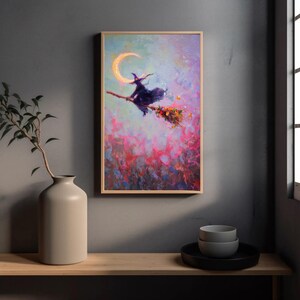 May include: A framed art print depicts a witch on a broomstick flying in front of a crescent moon. The witch is wearing a black hat and cloak. The background features a colorful, abstract blend of pink, purple, and blue hues.