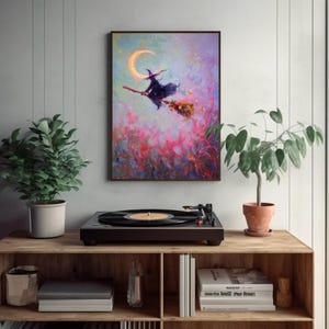 May include: A framed painting depicts a witch on a broomstick flying past a crescent moon. The artwork features a vibrant color palette of pinks, purples, and blues. The painting is displayed above a record player on a wooden shelf, with potted plants on either side.