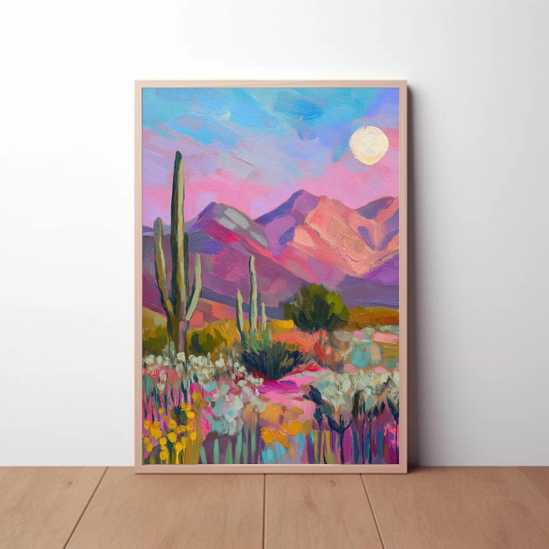 May include: A framed desert landscape painting with a vibrant color palette. The artwork depicts a desert scene with cacti, mountains, and a full moon. The sky transitions from blue to pink, and the foreground features colorful wildflowers.