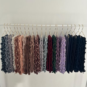 Può includere: Una collezione di 18 sciarpe arricciate in vari colori, tra cui grigio, rosa, marrone, bordeaux, verde e nero, appese a grucce dorate.