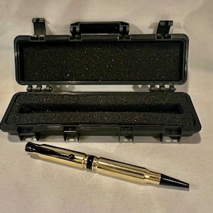 May include: A gold-colored pen made from a bullet casing with a black cap and clip. The pen is in a black hard plastic case with foam lining.