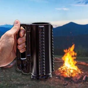 May include: A black ceramic mug with a unique, textured design is held in a hand. The mug has a large handle and a series of vertical ridges. The background shows a campfire, mountains, and a sunset.