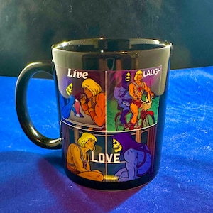 May include: Black ceramic mug featuring four panels with cartoon characters and the words "Live, Laugh, Love." The panels depict characters in various poses. The mug has a black handle and a glossy finish.