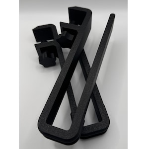 May include: Two black plastic clamps with a textured finish. The clamps are rectangular in shape with a small knob on the top.