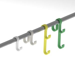 以下が含まれることがあります： 白、黄、緑のS字型フック4つが、直線のグレーの金属棒に掛かっています。各フックは、棒に固定される湾曲した上部ループと、アイテムを掛けるための2つの下部フックを備えた二股のデザインが特徴です。