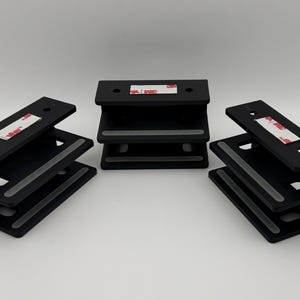 Peut inclure: Trois supports noirs en forme de Z avec des bandes adhésives. Chaque support comporte deux surfaces horizontales avec une bande antidérapante grise. Les supports sont disposés sur une surface blanche.