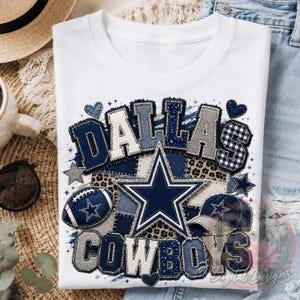 May include: A white t-shirt featuring a graphic design with the text DALLAS COWBOYS in a patchwork style. The design includes a large navy blue star, a football, a baseball cap, and small heart and star shapes in navy, grey, and leopard print.
