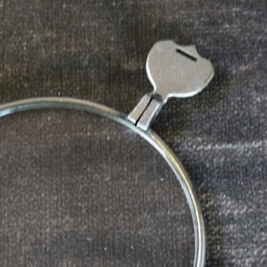 May include: A silver eyeglass frame with a round lens and a metal hinge. The hinge is shaped like a teardrop and has a small groove on the top.