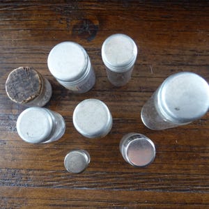 May include: A collection of eight small, clear glass bottles with silver lids. The bottles are arranged in a circle on a wooden surface.