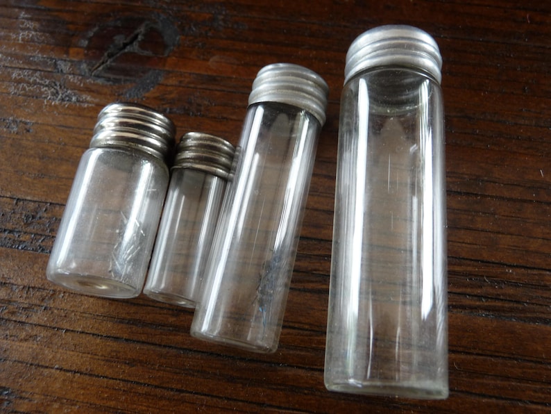May include: Four clear glass bottles with silver lids. The bottles are different sizes and are arranged in a row from largest to smallest.