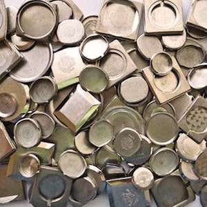 May include: A collection of various silver-toned watch components, including round, square, and rectangular shapes. The components are scattered, creating a textured, metallic surface. Some pieces have visible details, while others are plain.