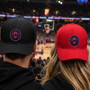 Peut inclure: Une casquette de baseball noire et une casquette de baseball rouge, chacune dotée d'un écusson circulaire sur le panneau avant. L'écusson présente un graphique stylisé de tête de dinosaure dans des tons violet, rouge et blanc, entouré d'étoiles.