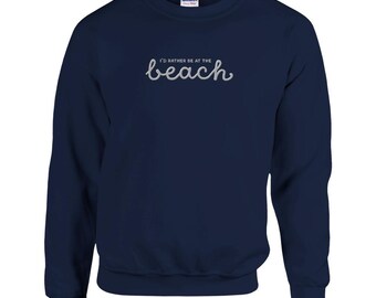 Op de afbeelding: Marineblauwe sweatshirt met de geborduurde tekst "I'd rather be at the beach" in een sierlijk lettertype. De sweatshirt heeft een ronde hals en lange mouwen. Het Gildan-merklogo is zichtbaar op de bovenrug.