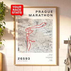 Op de afbeelding: Een ingelijste print van de routekaart van de Praagse Marathon, met een rode lijn die de route markeert. De print toont "PRAGUE MARATHON" en racegegevens: pace 9:33/mi, afstand 32,5 km en tijd 4:10:02. Een rode tekstballon leest "YOUR RACE STATS".